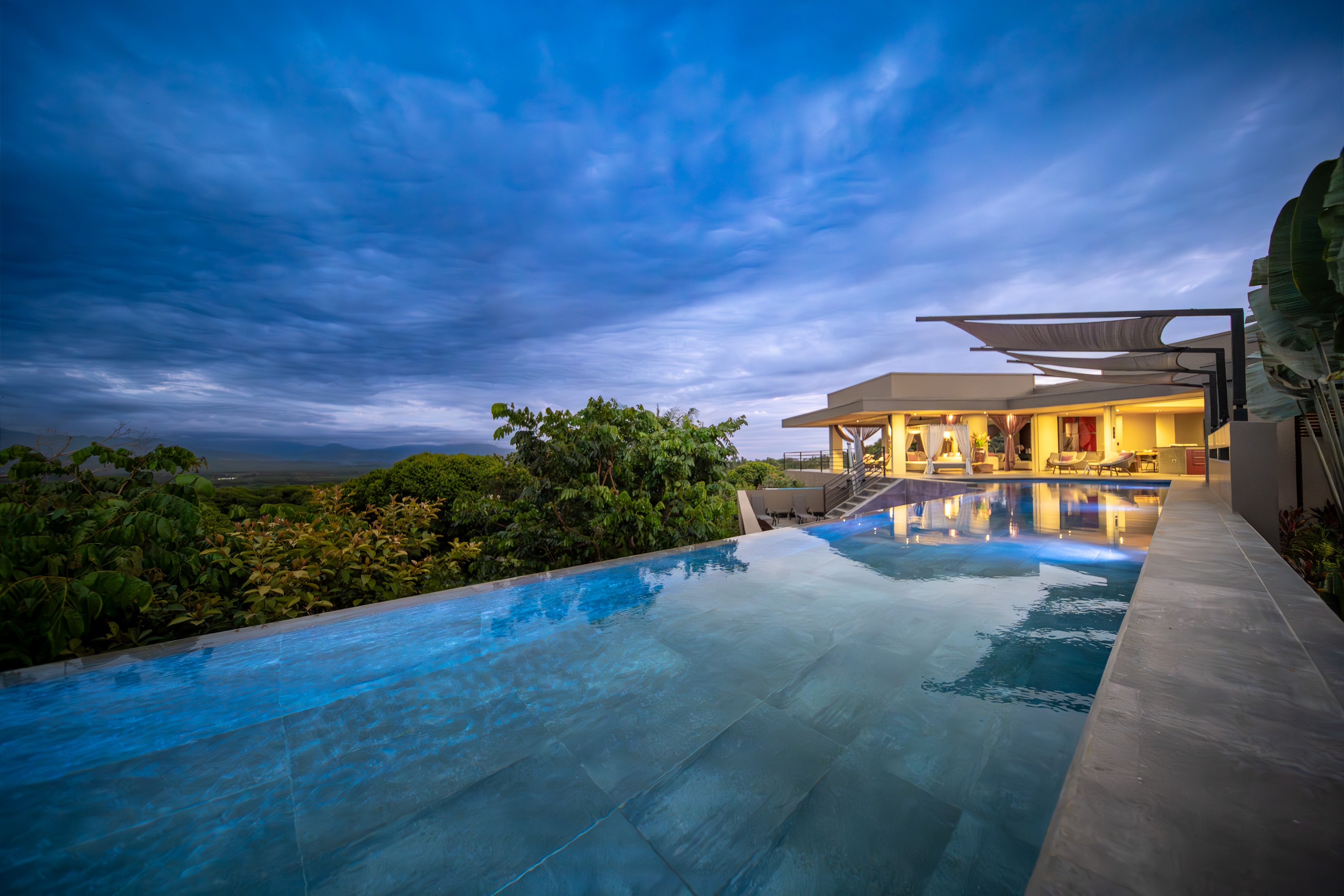 The infinity pool at dusk, running toward the lit house